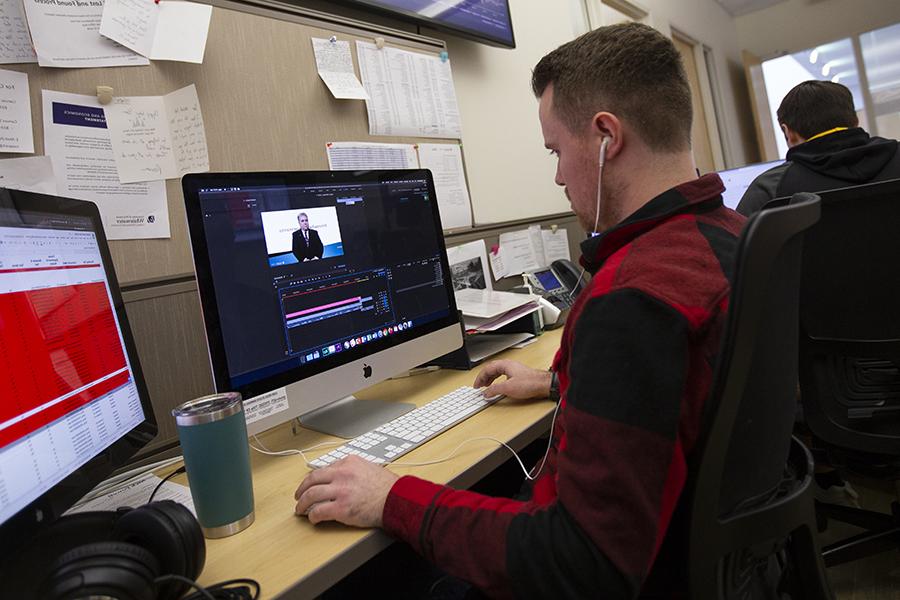 A student wears headphones while working on a Mac computer.