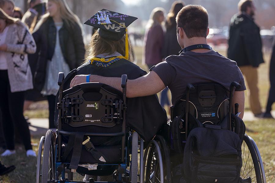 Two people in wheelchairs with their arms each other at graduation.